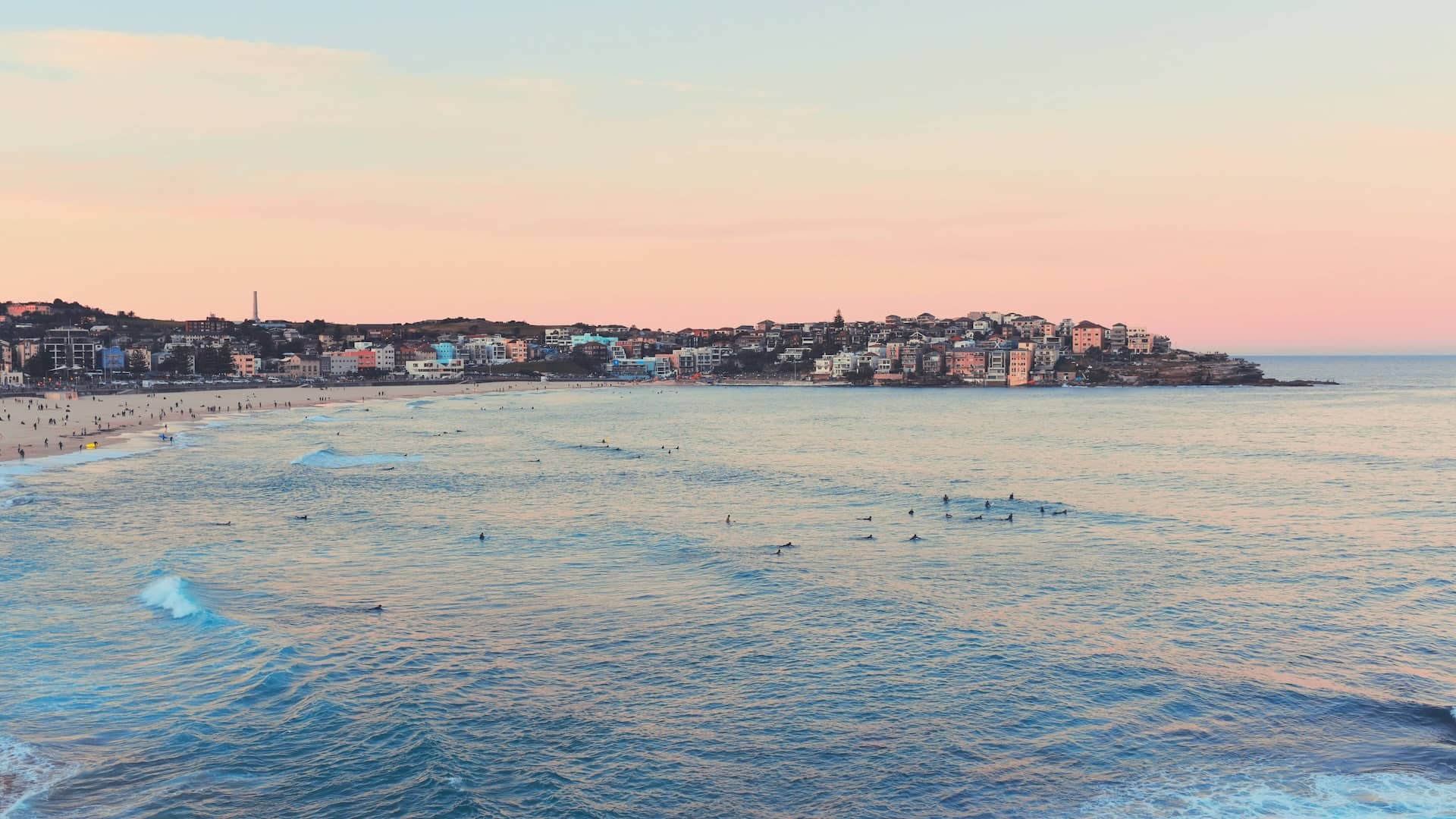 Bondi coastline with buildings and people in the water at sunset.